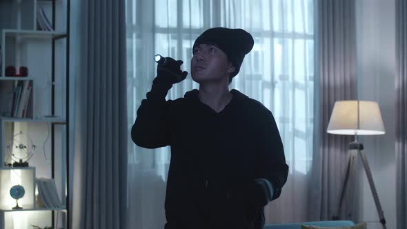 Asian Thief Man Holding Flashlight Looking Around And Putting A Mask Down While Walking alt