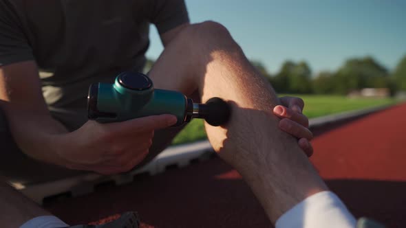 Athletic Male Massages Muscles with Hand Massage Gun Recovering From Stadium Running Workout alt