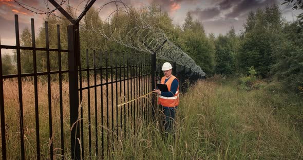 Worker with a Measuring Tape Measure a Fence with Barbed Wire