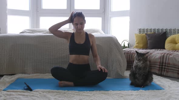 Young Woman Blogger Shoots Video Doing Yoga Exercise with Phone While Maine Coon Cat is Sitting Side