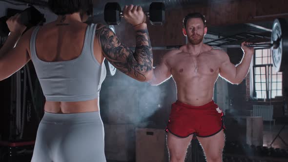 Adult Couple in the Gym  Athletic Man and Tattooed Woman Pumping Their Muscles Using Dumbbells alt