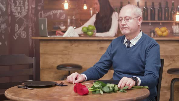 Sad Old Man Sitting at a Table in a Restaurant and Waiting for His Date alt