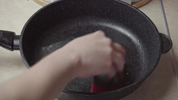 Hand with a foam sponge washes a dirty frying pan. Wash the pan with a sponge alt
