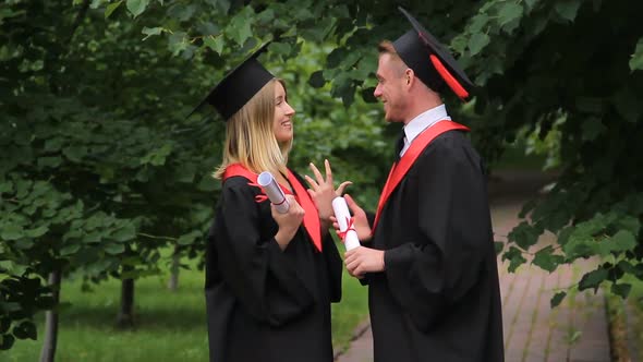 Excited Smiling Graduates Holding Diplomas and Talking About Future in Park alt