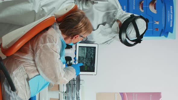 Vertical Video Dentist in Coverall Examining Xray Image on Tablet alt