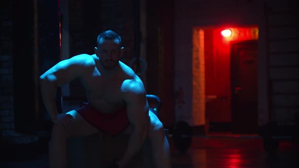 Tough Man Pumping His Biceps in Contrast Lighting and Looking in the Camera alt