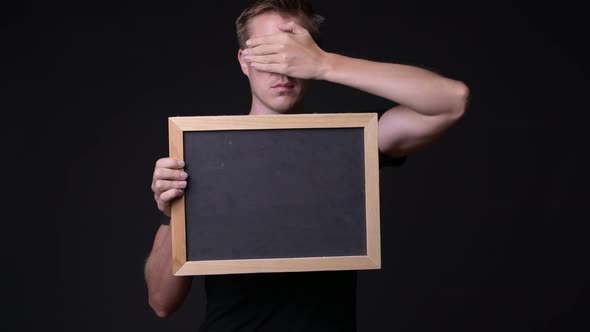 Young Handsome Man Holding Blackboard Against Black Background alt