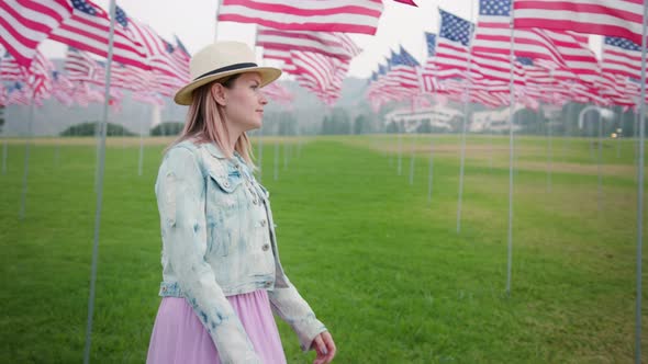 Young Woman in the Urban Green Park with Many American Flagpoles Blowing in Wind alt