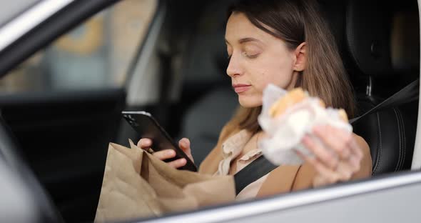 Woman Typing on a Smart Phone While Having a Snack in a Vehicle alt