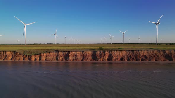 Windmills on a cliff above the sea, top view. Wind farm with turbine cables for wind energy.