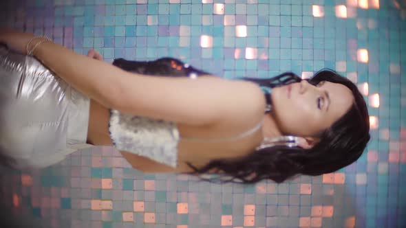Portrait of a Sexy Brunette Woman with Earrings and a Silver Top on Shiny Background in the Studio