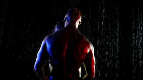 Couple with Golden Metallic Skin Stands in Streams of Water on a Black Background alt