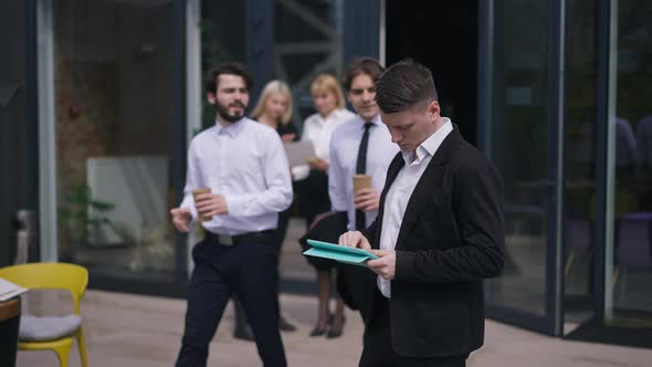Thoughtful Young Caucasian Male Employee Standing on Sunny Office Terrace with Tablet Planning alt