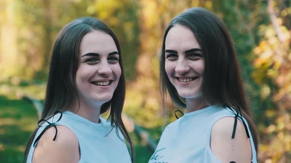 Twins Girls Smiling and Look at Camera in Green Nature Background. Slow Motion alt