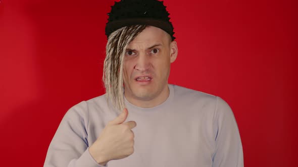 Young puzzled man with dreadlocks in black cap pointing finger at you in camera alt