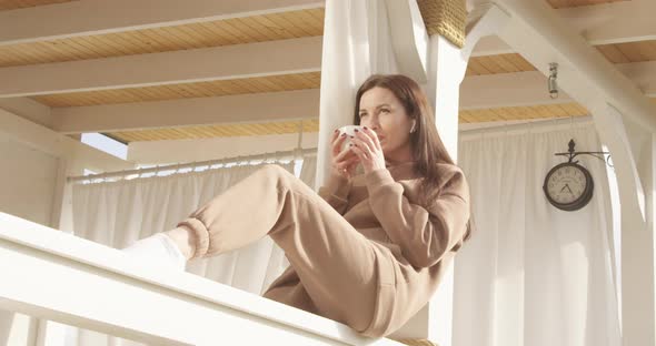 Woman Sitting On A Terrace Deck Listening To The Music And Drinking Coffee In The Morning With Sun alt