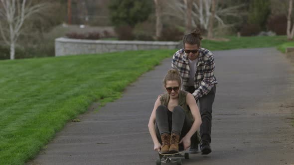 Teen pushing girl on skateboard at park