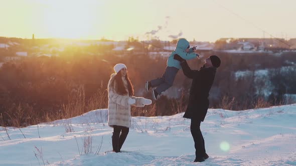 Family Entertains on White Snow Ground Against Blurry Roofs alt