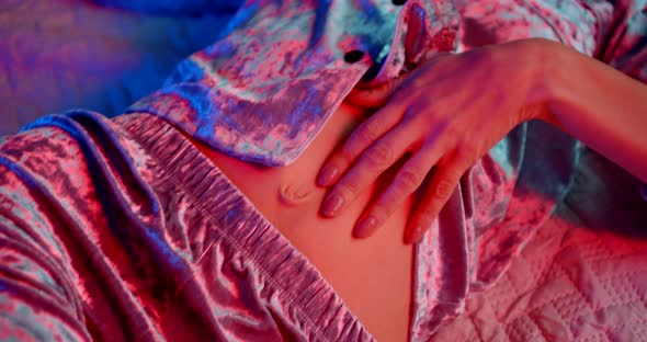 a Woman's Body in Pajamas Is Lying in Bed. the Woman Pats Her Stomach. the Camera Is Moving. the alt