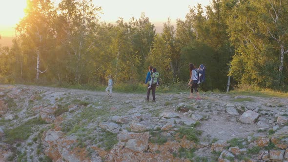 Young Parents with Three Children Walk Along a Mountain Path at Sunset