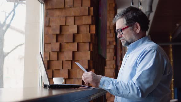 Senior Man Studies Documents Sitting in a Cafe alt