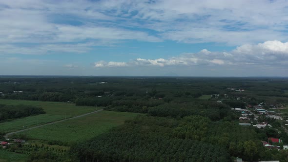 Aerial panning shot of Cu Chi, Vietnam with farms, forests on sunny day with blue sky. alt
