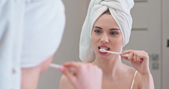 Young Female Stands in Front of the Mirror in Her Bathroom and Brushing Her Teeth, Care of the Oral alt