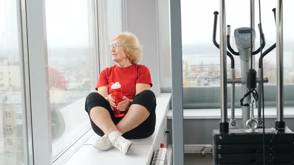 Pretty Active Retired Woman in Red Tshirt Sitting on Window Sill in Gym alt