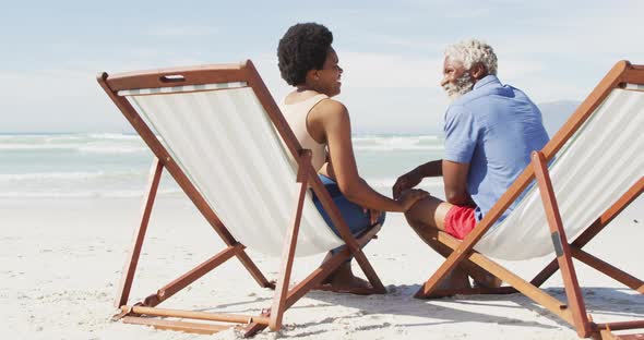 African american couple holding hands and lying on sunbeds on sunny beach alt