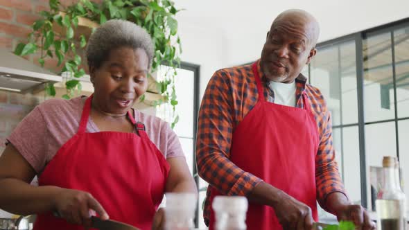 Happy african american senior couple cooking together in kitchen alt