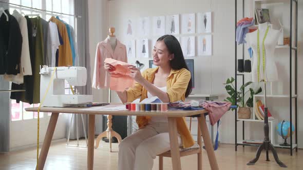Asian Female Designer With Sewing Machine Holding And Looking At The Fabrics While Designing Clothes alt