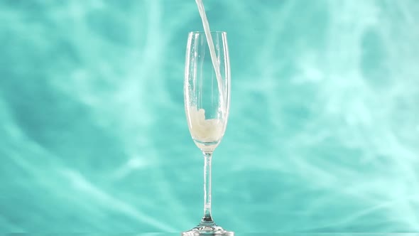Yellow Soda Water is Pouring Into Champagne Flute Glass Standing Over Smoky Cyan Background alt
