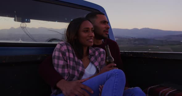 Young couple on a road trip sitting outside on their truck at dusk alt