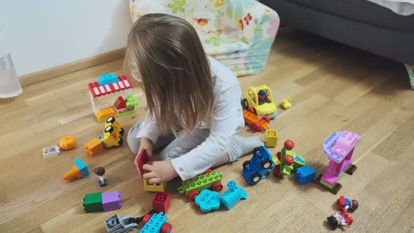 Cute Little Girl Sitson Floor and Playing with Colorful Building Blocks