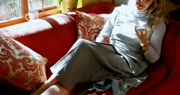 Mature woman writing on diary while talking on mobile phone 4k alt