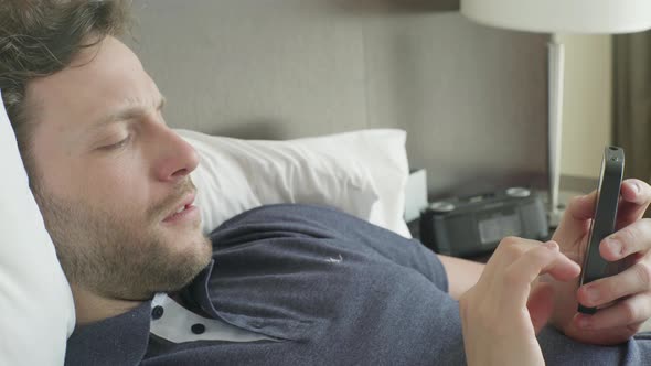 Man lying in bed looking at smart phone