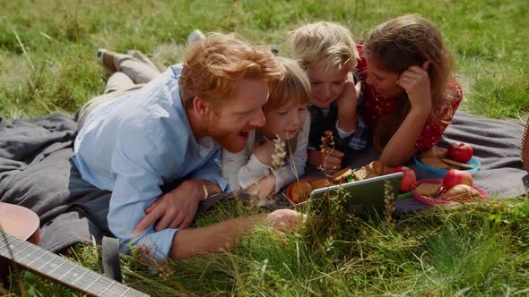 Family Watching Tablet Computer on Picnic Lying Green Grass alt