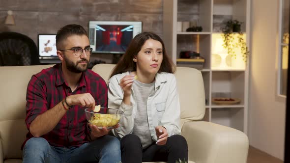 Caucasian Young Couple Eating Chips While Watching TV alt