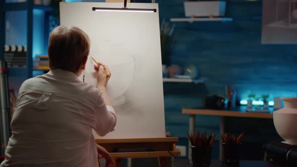 Female Artist in Retirement Age Using Pencils to Draw Vase Artwork alt