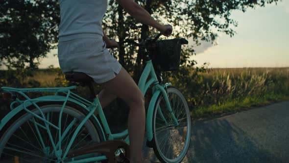 Side view of unrecognizable caucasian woman riding a bike on sunset on village road. Shot with RED h alt