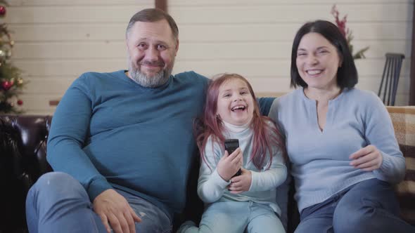 Carefree Friendly Caucasian Family Watching Comedy Movie on TV at Home. Front View Portrait of alt