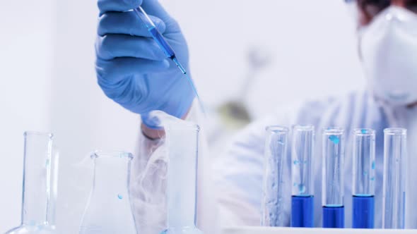 Close Up Handheld Footage of Chemist Pouring Solution with Pipette in a Reactive Blue Liquid alt