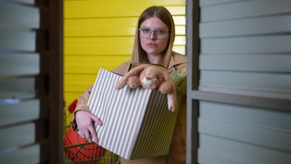 Shooting From Inside Locker Room of Young Woman Opening Door Standing with Box alt
