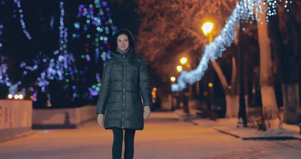 Happy Young Woman Walks on a City Street in Winter Garlands of Lights are Burning alt