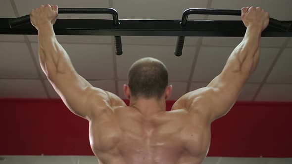 Bodybuilder with perfect muscular body doing pull-ups, preparing for competition alt