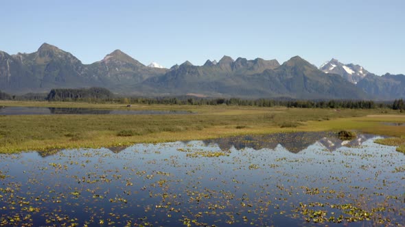 Scenic View With Reflections Of Snowcapped Mountains Against Blue Sky In Alaska, USA. - Wide Shot alt