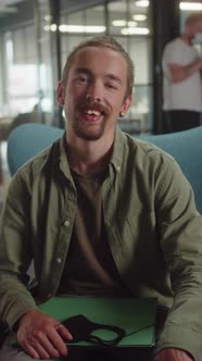 A Young Caucasian Man is Sitting on the Chair in the University Smiling and Looking at the Camera alt