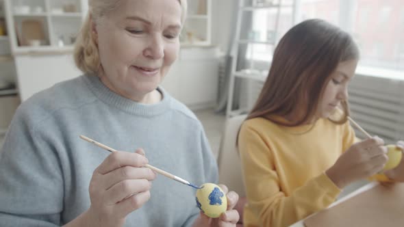 Cheerful Senior Woman and Granddaughter Decorating Easter Eggs alt