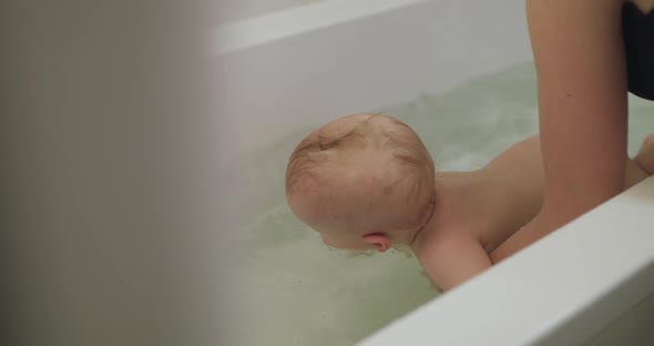 Cute Blueeyed Infant Lying in a Bath on Mother's Hands and Cognizing Arounds alt