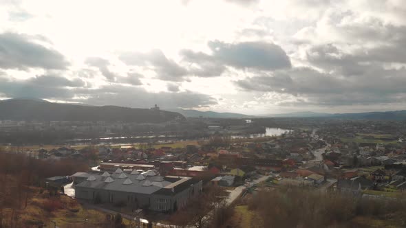 Forward Aerial Drone over outskirts of small city with silhouette castle on hill in background alt